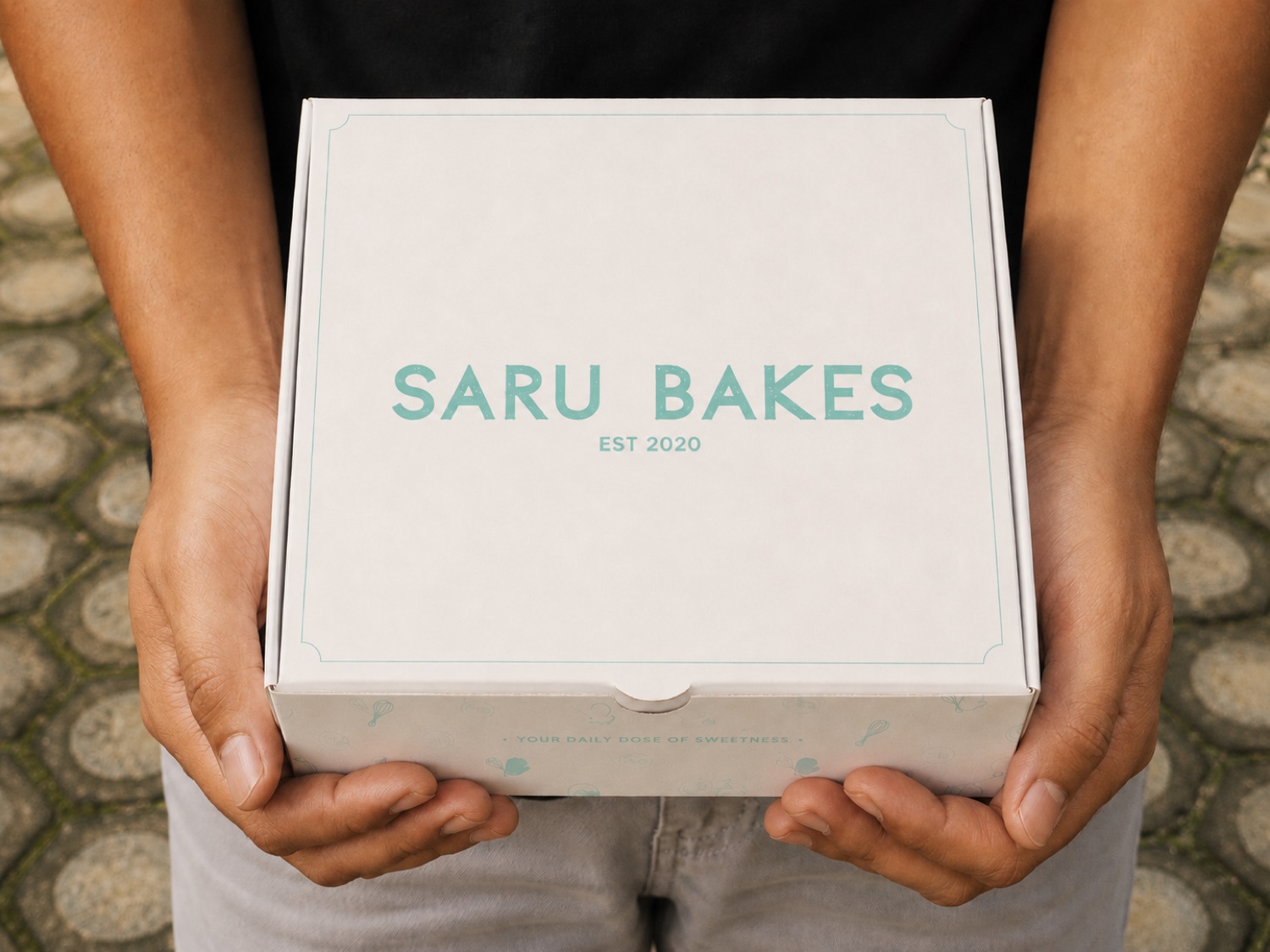 Saru Bakes classic box — mint logo on cream, “Est 2020”, held in hand
